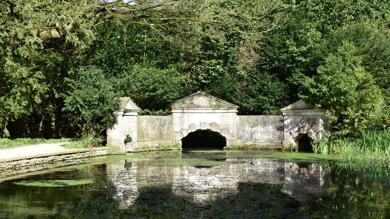A reflection of the Sham Bridge in the Serpentine Lake with trees behind